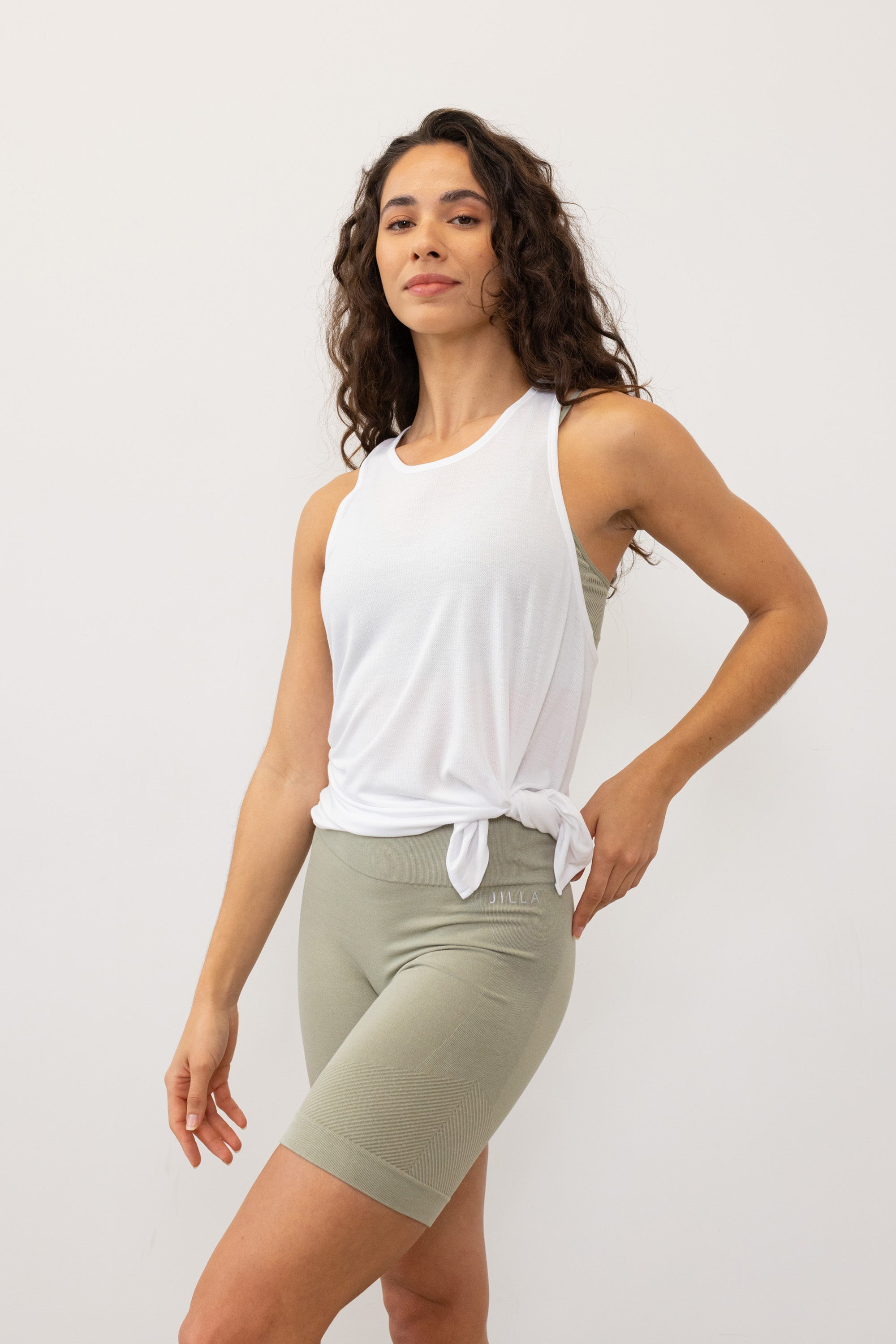 Stay cool and comfortable in the white Revolve Bamboo Tank Top from Jilla Active. Crafted from a bamboo blend, it's perfect for warm days and workouts. With a seamless knit for a smooth fit, side split for versatile styling, and twisted racerback for maximum movement, it's ideal for studio classes, runs, or gym sessions.